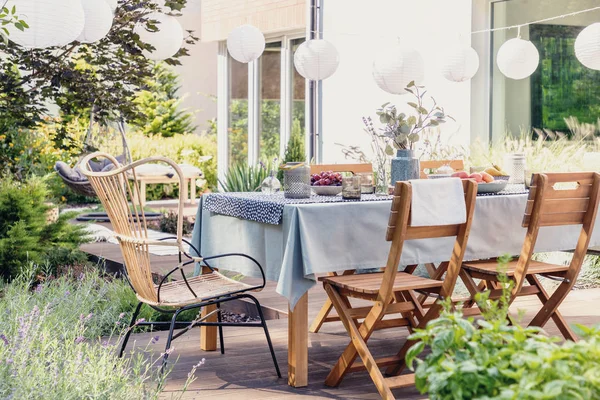 Table with wooden chairs in bright green garden of modern house, real photo — Stock Photo, Image