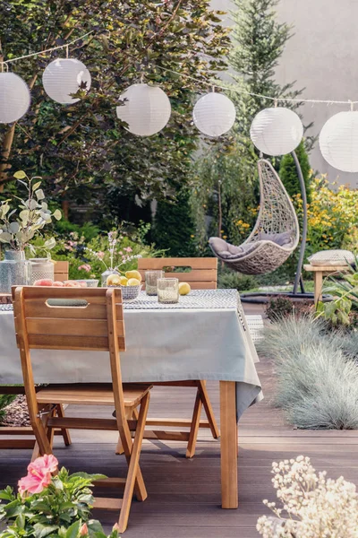 White paper lamps above garden table with chairs on stylish terrace with wooden floor and plants — Stock Photo, Image