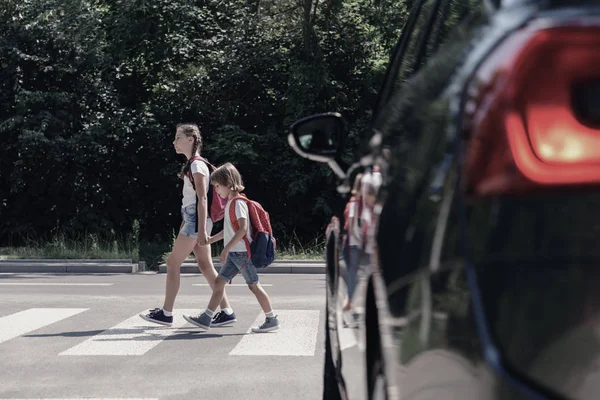 Lage hoek op de auto in de voorkant van kinderen met rugzakken lopen door zebrapad naar de school — Stockfoto