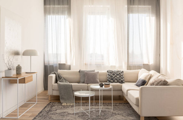 Бежевый удобный угловой диван с серыми подушками в элегантном интерьере гостиной с белой стеной
