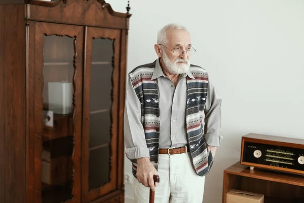 悲伤的老人拿着拐杖独自站在家里 — 图库照片
