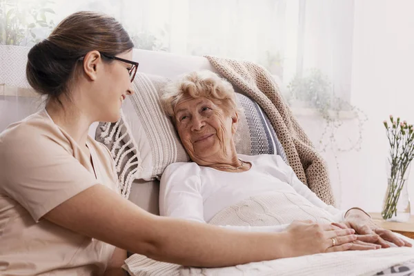 Elderly woman in hospital bed with social worker helping her — Stock Photo, Image