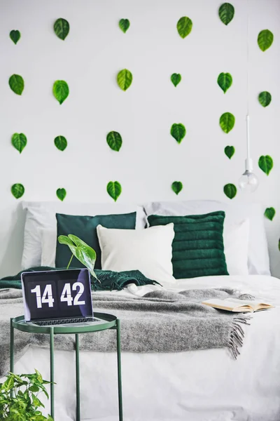 Interno bianco della camera da letto con letto king size, foglie verdi giungla urbana sulla parete e piccolo computer portatile sul tavolino — Foto Stock