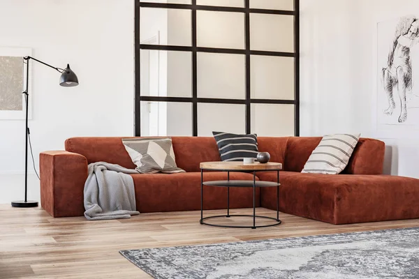 Стильный коричневый угловой диван с узорчатыми подушками в элегантном интерьере гостиной с многолионной стеной — стоковое фото
