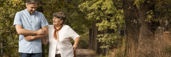 Panoramic view of grey senior lady with walking cane in the garden with volunteer — Stock Photo, Image