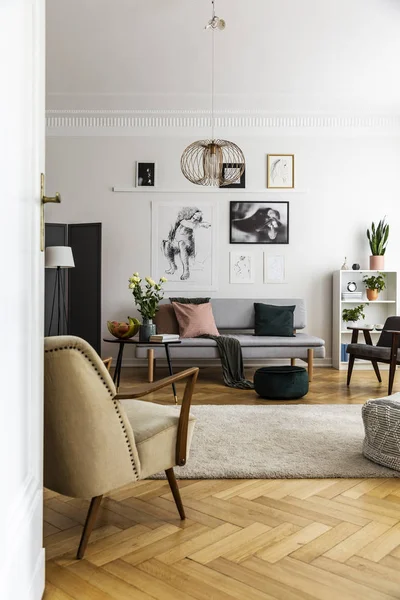 Sillón junto a la alfombra y flores en el interior de la sala de estar con carteles encima del sofá. Foto real — Foto de Stock