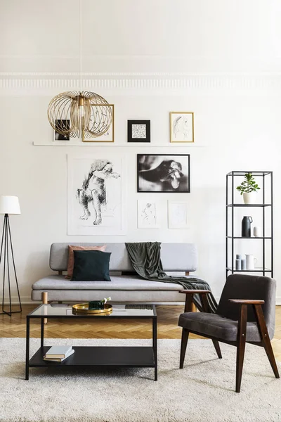 Armchair next to table on carpet in white living room interior with posters and lamp. Real photo — Stock Photo, Image