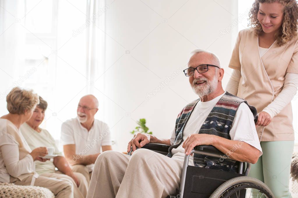 Senior man on wheelchair with helpful caregiver supporting him