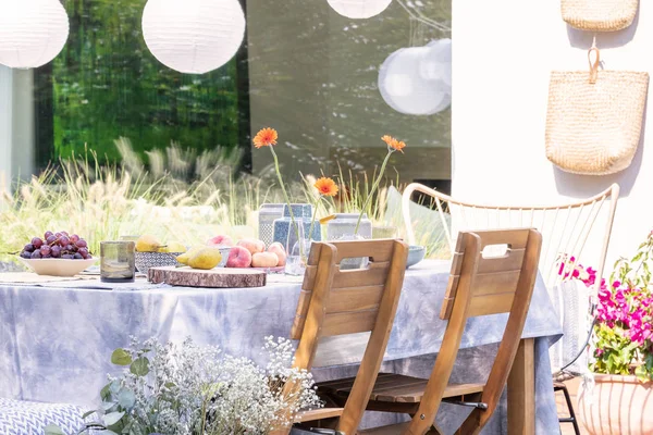 Sedie in legno a tavola con cibo sulla terrazza della casa con fiori e lampade — Foto Stock