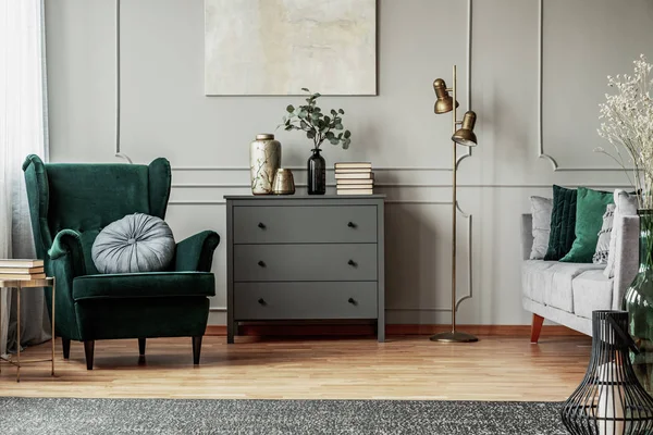 Abstrakte Malerei an grauer Wand o zeitgenössisches Wohnzimmerinterieur mit smaragdgrünem Sessel mit rundem Kissen, Kommode und Couch — Stockfoto