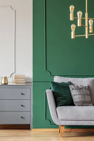 Green wall, grey Scandinavian couch and wooden chest of drawers in elegant living room interior
