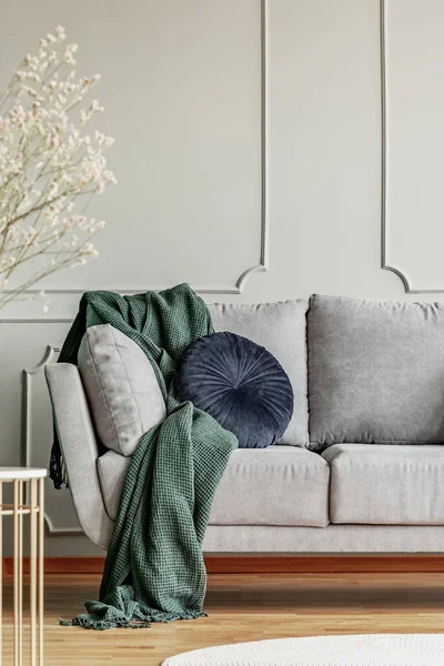 Navy blue pillow and emerald green blanket on grey sofa in elegant living room interior