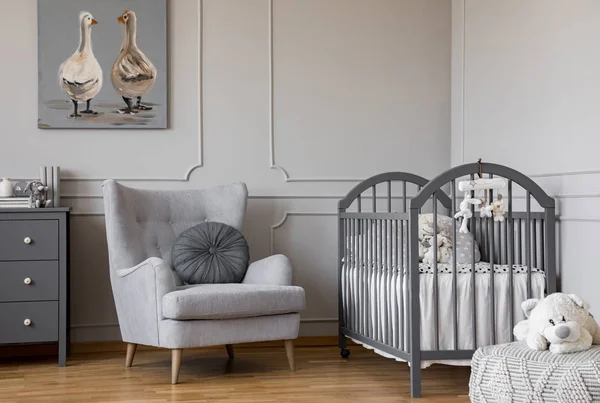 Ducks on cute oil painting in tasteful baby room with grey armchair and wooden crib, copy space on empty wall — Stock Photo, Image