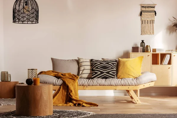 Divano scandinavo con cuscini e coperta giallo scuro in luminoso soggiorno interno con lampadario nero — Foto Stock