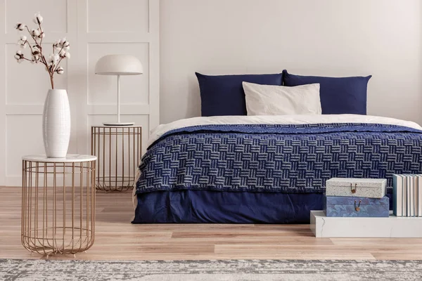Blommor i vas på nattduksbord bredvid King size säng med marinblå sängkläder — Stockfoto
