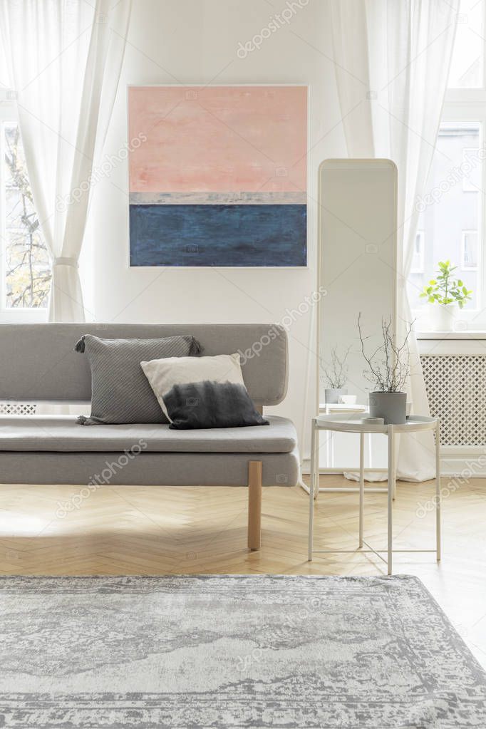 Fashionable settee with pillows in bright living room interior with pastel pink and blue painting