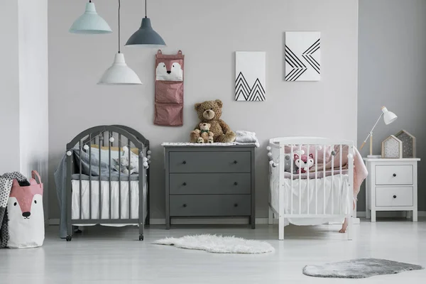 Brown teddy bear on grey wooden commode between two cribs in fashionable bedroom for twins — Stock Photo, Image