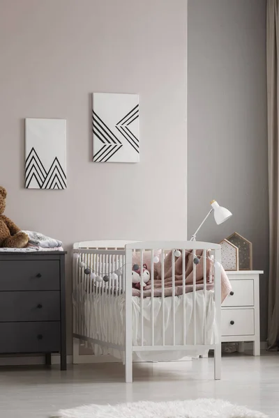 Vista vertical de la cuna blanca con ropa de cama de color rosa pastel y bolas de algodón en gris y beige dormitorio de bebé de moda —  Fotos de Stock