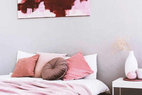 Круглая бежевая подушка на белой кровати в стильном интерьере спальни с абстрактной росписью на стене — стоковое фото