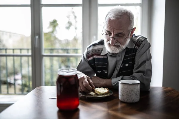 Abuelo mayor con cabello gris y barba sentado solo en la cocina desayunando —  Fotos de Stock