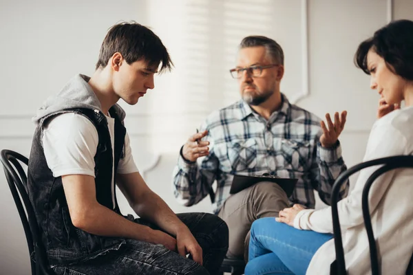 Sad teenager listening to his psychatrist during visit in mental hospital with his mother — Stock Photo, Image