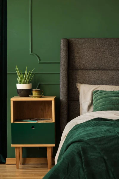 Πραγματική φωτογραφία ενός κομοδίνο δίπλα σε ένα κρεβάτι σε ένα σκούρο πράσινο υπνοδωμάτιο εσωτερικό — Φωτογραφία Αρχείου