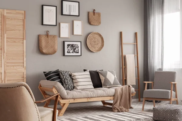 Модное винтажное кресло рядом с шикарным скандинавским диваном с подушками в стильном интерьере гостиной — стоковое фото