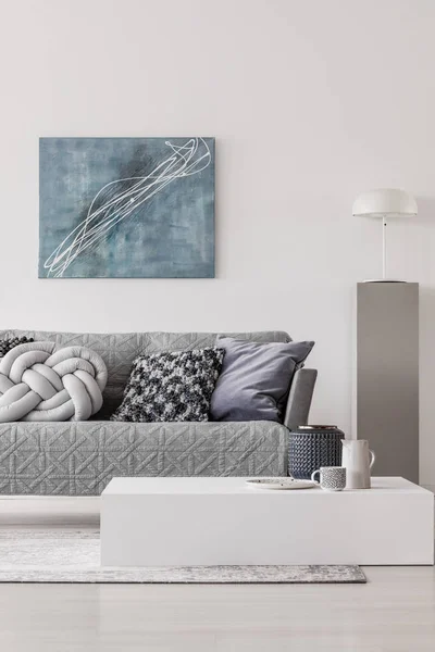 Синяя абстрактная живопись на белой стене современного интерьера гостиной с серым диваном с подушками — стоковое фото
