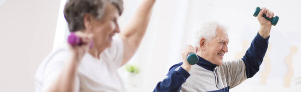 Панорама с двумя улыбающимися пожилыми людьми, тренирующимися в реабилитационном центре
