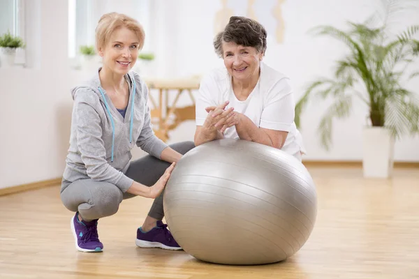 Fisioterapeuta sorridente com mulher idosa deitada em bola de exercício durante a fisioterapia — Fotografia de Stock