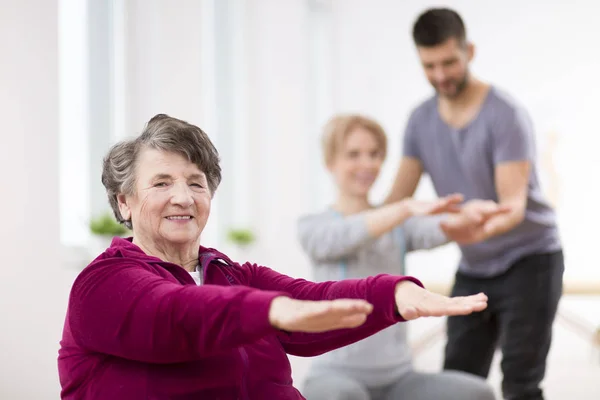 Senior Lady traint tijdens groep fysiotherapie in revalidatiecentrum — Stockfoto