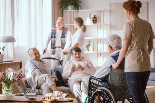 UngSjuksköterska tar handikappade Senior man på rullstolen till h — Stockfoto