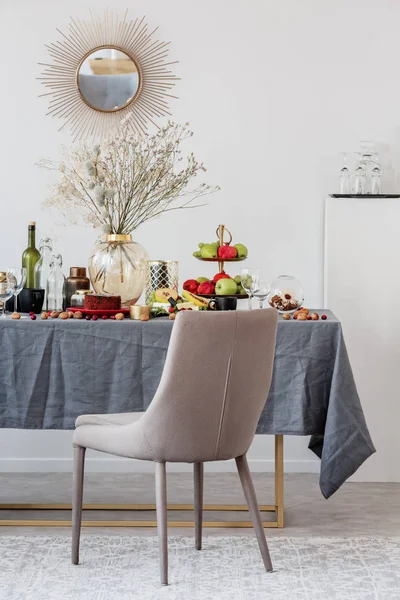 Стильний стілець поруч з обіднім столом з їжею, фруктами та квітами — стокове фото