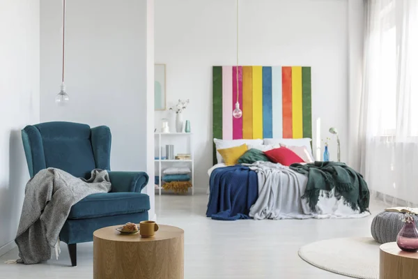 Fauteuil confortable avec couverture grise dans une chambre colorée avec lit king size et tête de lit multicolore — Photo