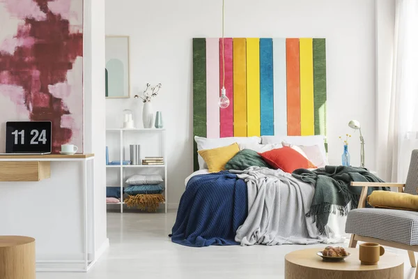 Testiera colorata in letto king size con cuscini e coperta e home office con laptop e vaso con fiori — Foto Stock