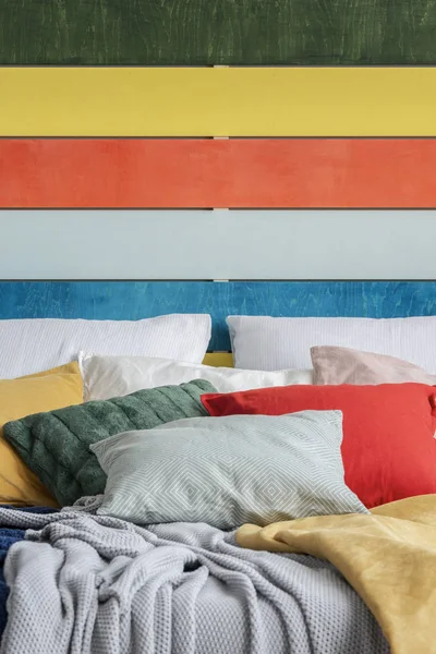 Parede de madeira colorida atrás da cama com travesseiros cinza, vermelho, amarelo e verde — Fotografia de Stock