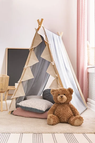 Vertical view of teddy bear next to tent with pillows in cute child\'s playroom, real photo