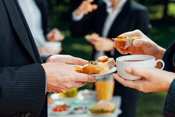 Closeup of businesspeople eating coffee and sandwiches during outdoor business lunch — Stock Photo, Image