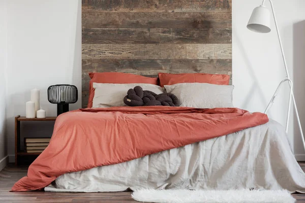 Удобная двуспальная кровать с деревянным ржавым изголовьем и белой промышленной лямкой рядом с ней — стоковое фото