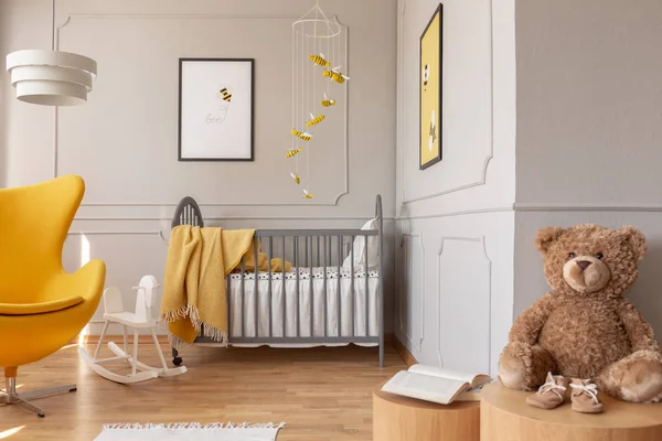 Teddy bear, crib and yellow armchair in a toddler room interior. Real photo — Stock Photo, Image