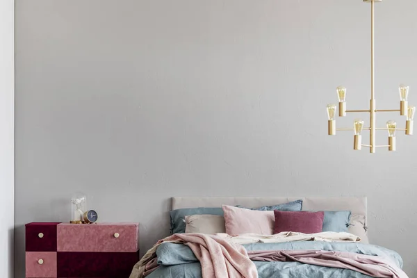 迪丝绒覆盖柔和的粉红色和酒红色床头柜旁边温暖的床与蓝色和米色床上用品和粉红色枕头 — 图库照片