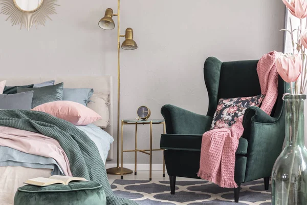 Květinové polštáře a růžová přikrývka na smaragdově zeleném pohodlném křesle v elegantní ložnici — Stock fotografie