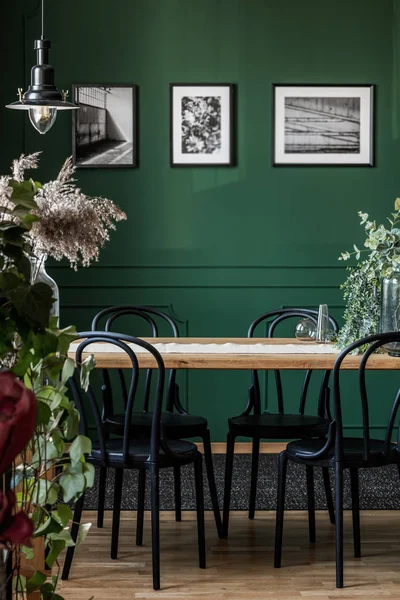 Foto reale di sedie nere in piedi su un tavolo di legno in elegante sala da pranzo interno con foto incorniciate sulla parete verde — Foto Stock