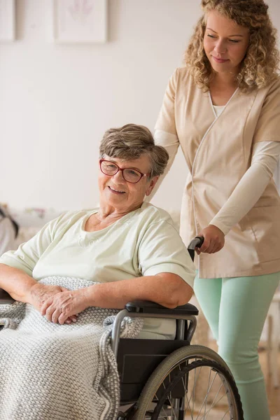 Pozytywny starszy pacjent na wózku inwalidzkim z pielęgniarką wspomagającą — Zdjęcie stockowe