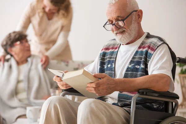 Senior man på rullstol läsa en bok — Stockfoto