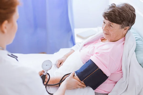 Mujer mayor con monitor de presión arterial en su brazo y joven interno en el hospital — Foto de Stock