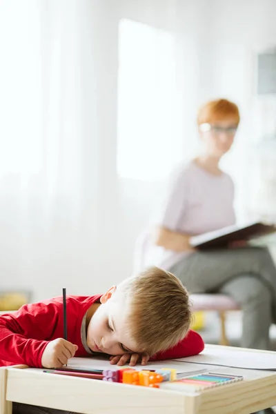 穿着红色毛衣的悲伤的小男孩通过做学习,这意味着画画、玩耍和交谈 — 图库照片