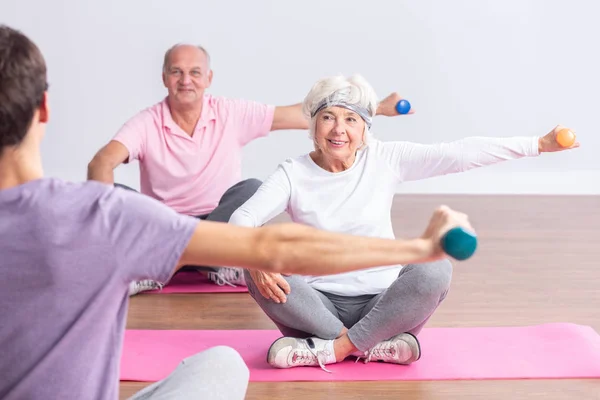 Pareja de personas mayores activas durante los ejercicios en el gimnasio con un instructor joven —  Fotos de Stock