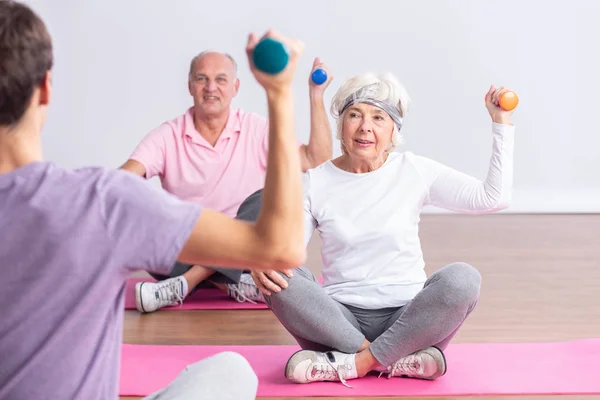 Actieve senioren zittend op yogamatten die de halters optillen tijdens fitnesslessen — Stockfoto