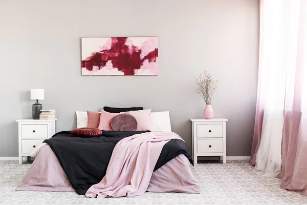 Flower in pastel pink vase on white wooden nightstand next to king size bed in trendy bedroom interior